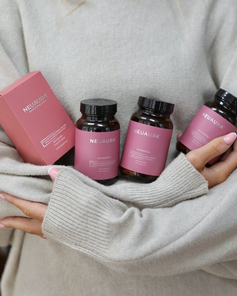 A close-up, high-quality shot of a woman holding branded intimate supplement bottles against a soft knit sweater background.